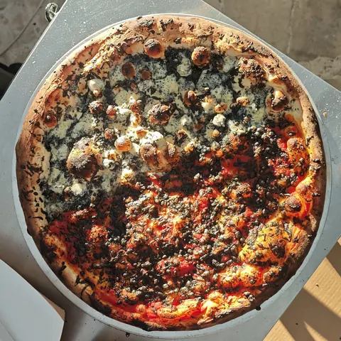 heavily charred burnt. sourdough pizza with bubbling cheese and a dark crumbled topping, top view